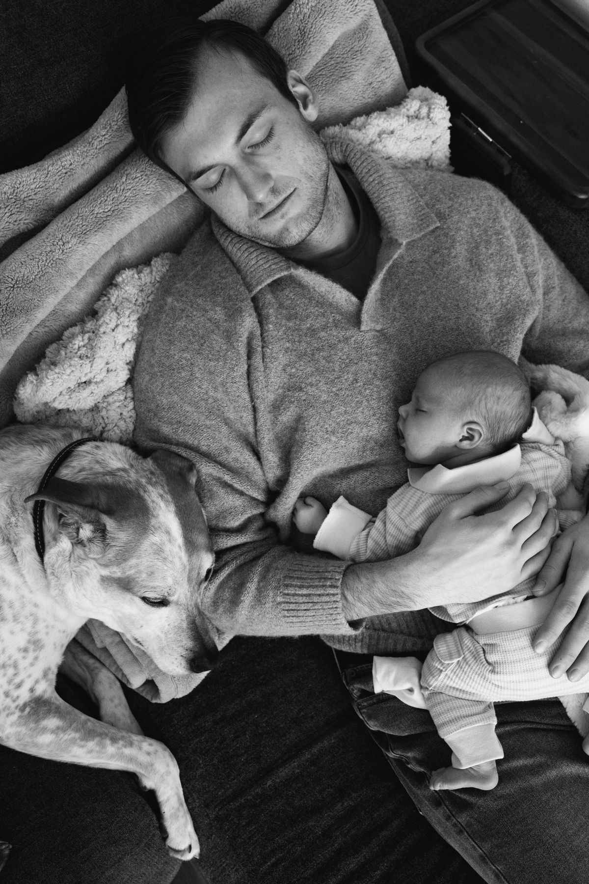 Father, newborn and dog asleep on the sofa, in black and white