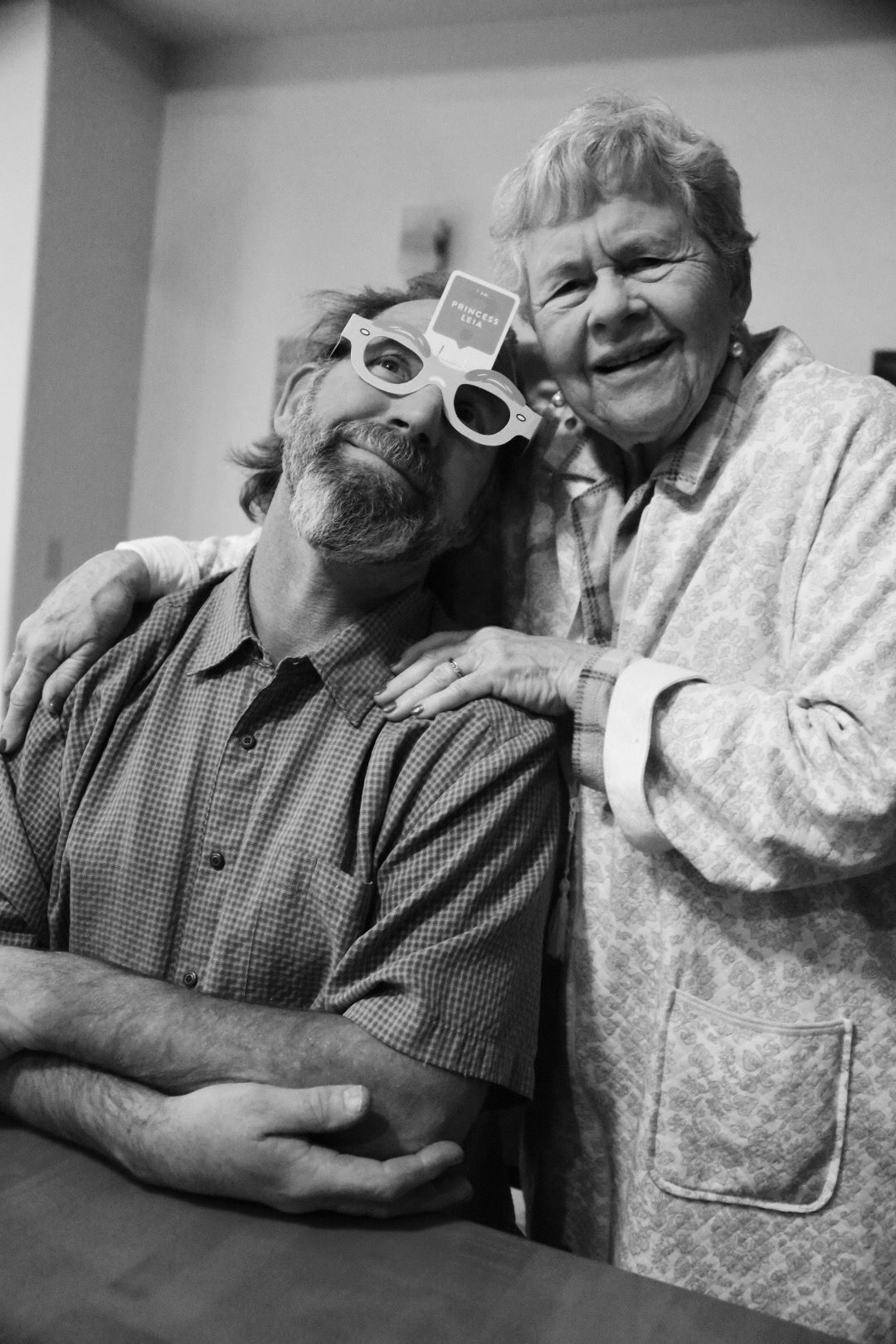 Two people laughing, one in novelty glasses, in black and white